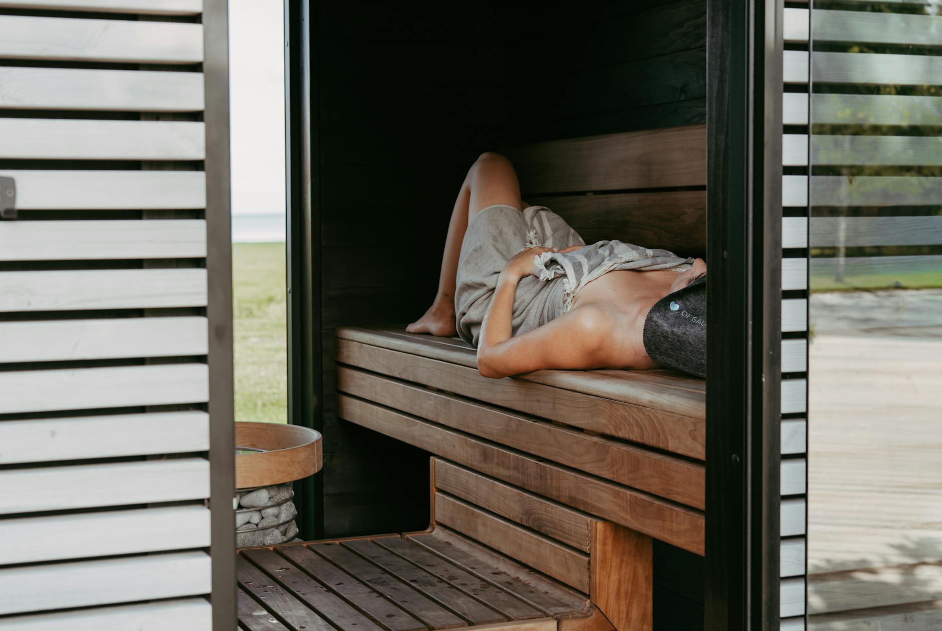 Osoba odpoczywająca w nowoczesnej saunie w czapce i ręczniku